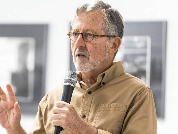 Elias Crim speaking into microphone during presentation, wearing tan shirt