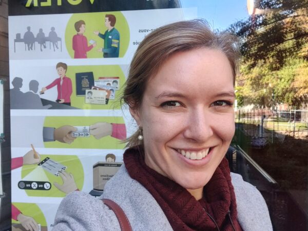 Marion Pellegrin smiling selfie outside polling station poster