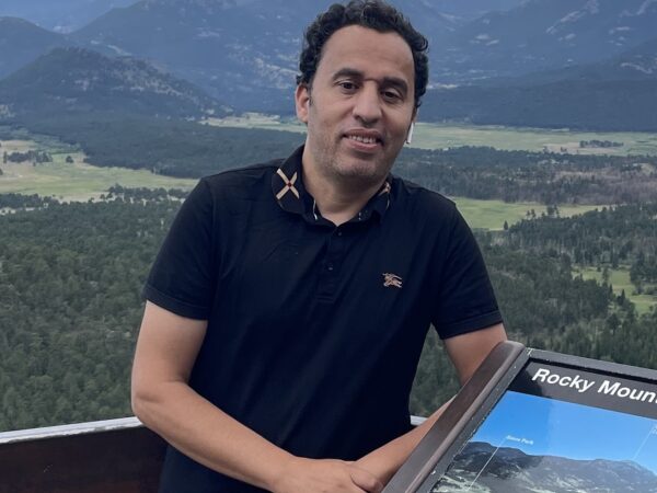 Ahmed Armani smiling at Rocky Mountain overlook with scenic peaks background