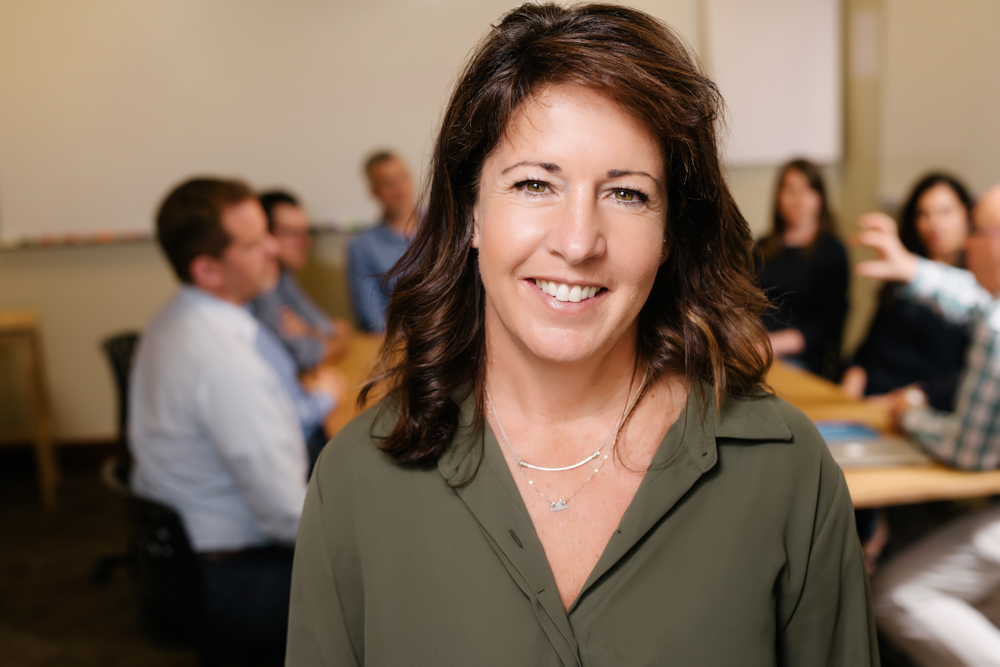 Fotografía profesional de Jennifer Briggs, sonriendo en un aula. {{brizy_dc_image_alt entityId=