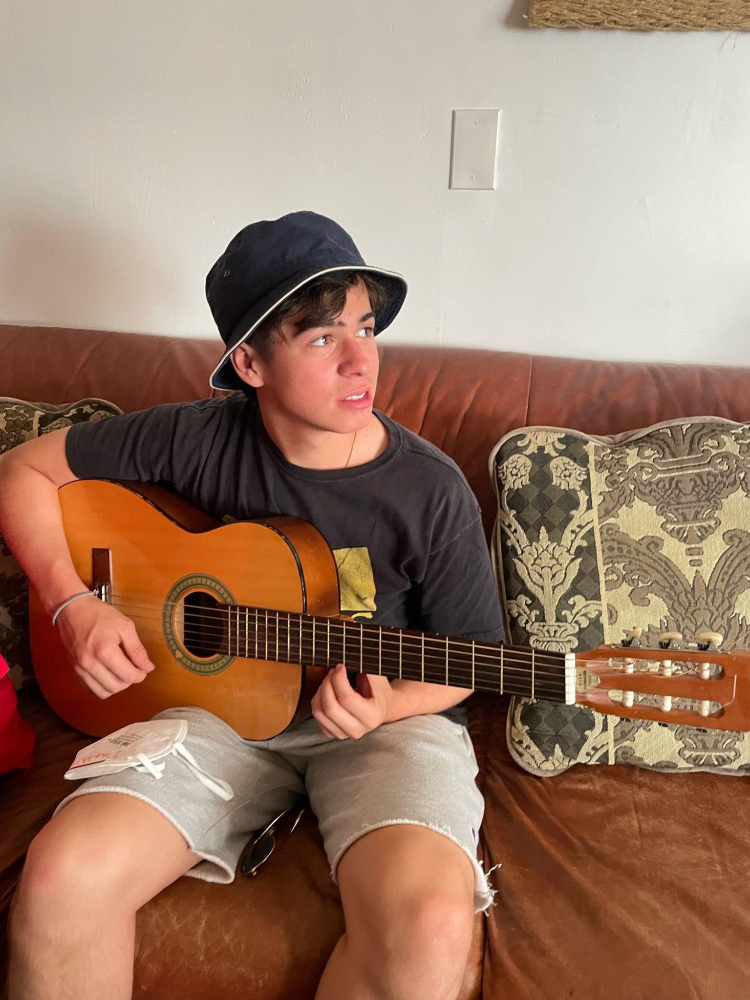 Danny playing acoustic guitar on couch wearing bucket hat
