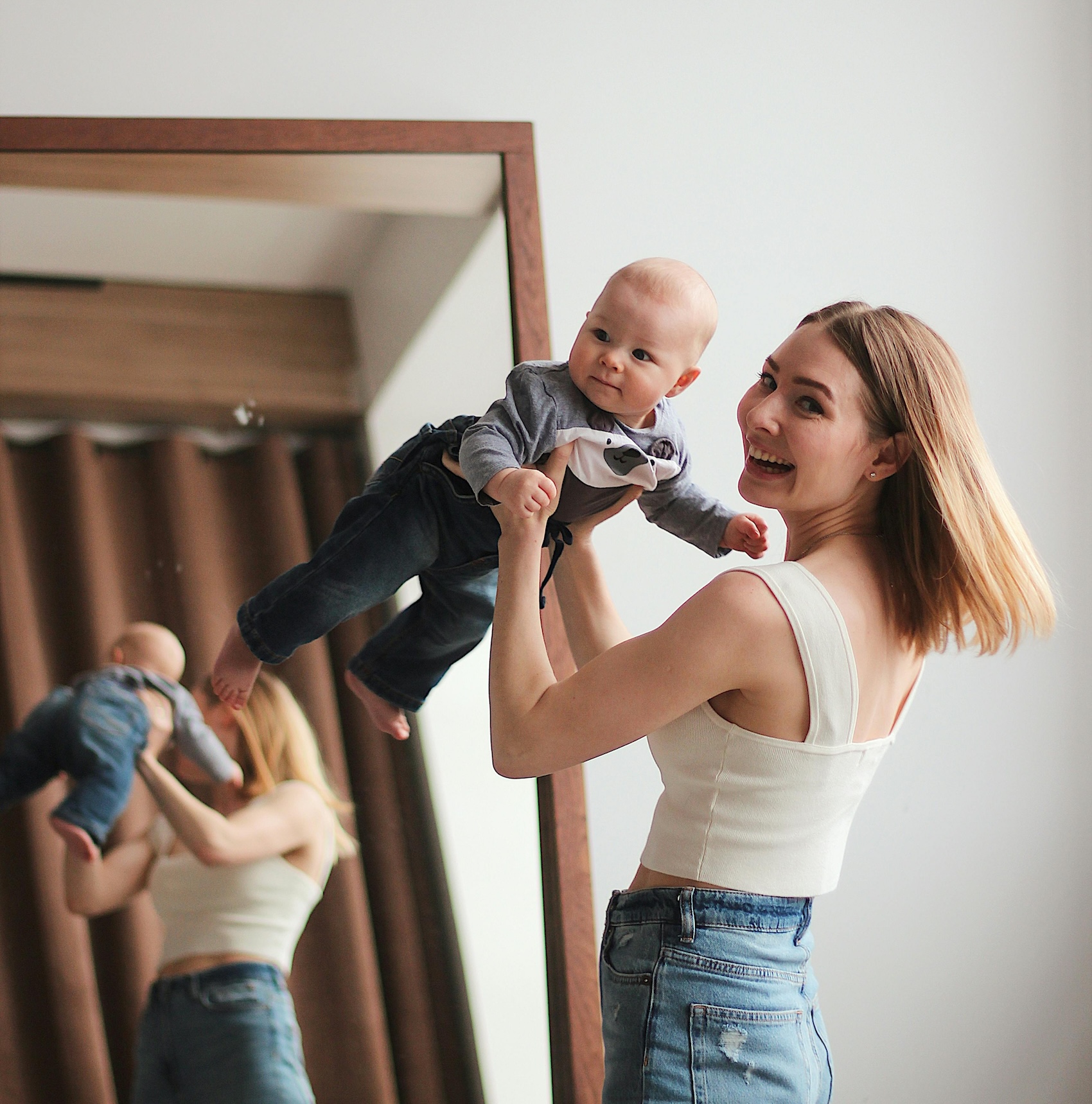 Mother lifting smiling baby in front of mirror at home