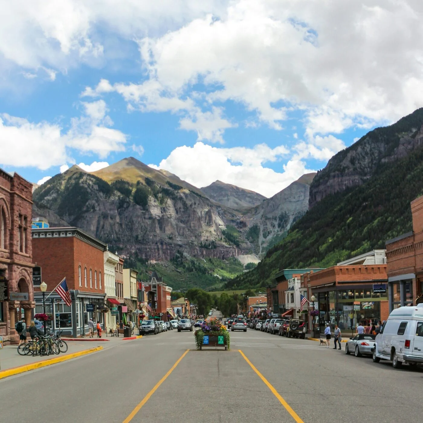 Main street of small mountain town with cars and shops, dramatic rocky peaks background