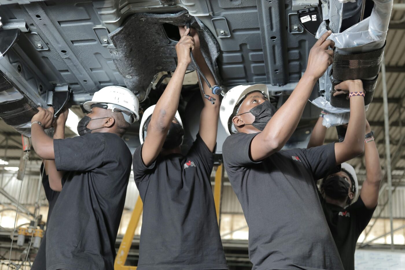 Three auto mechanics in hard hats working under car lift in garage