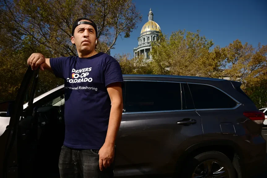 Male driver wearing Drivers Coop Colorado shirt standing by car in front of Colorado Capitol