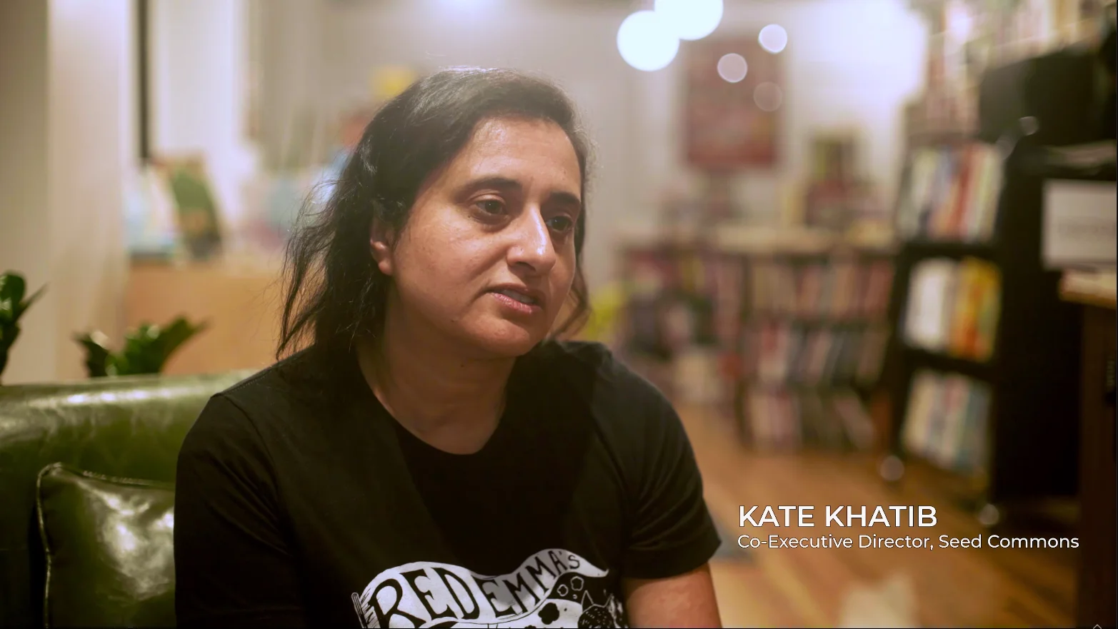 Kate Khatib speaking on Seed Commons video, seated on couch in library background
