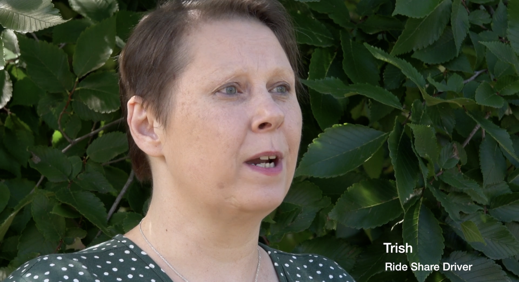 Trish, rideshare driver, speaking outdoors in front of leafy background