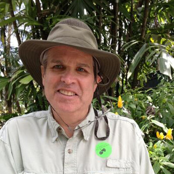 Roy Morrison smiling in safari hat and khaki shirt, lush garden background