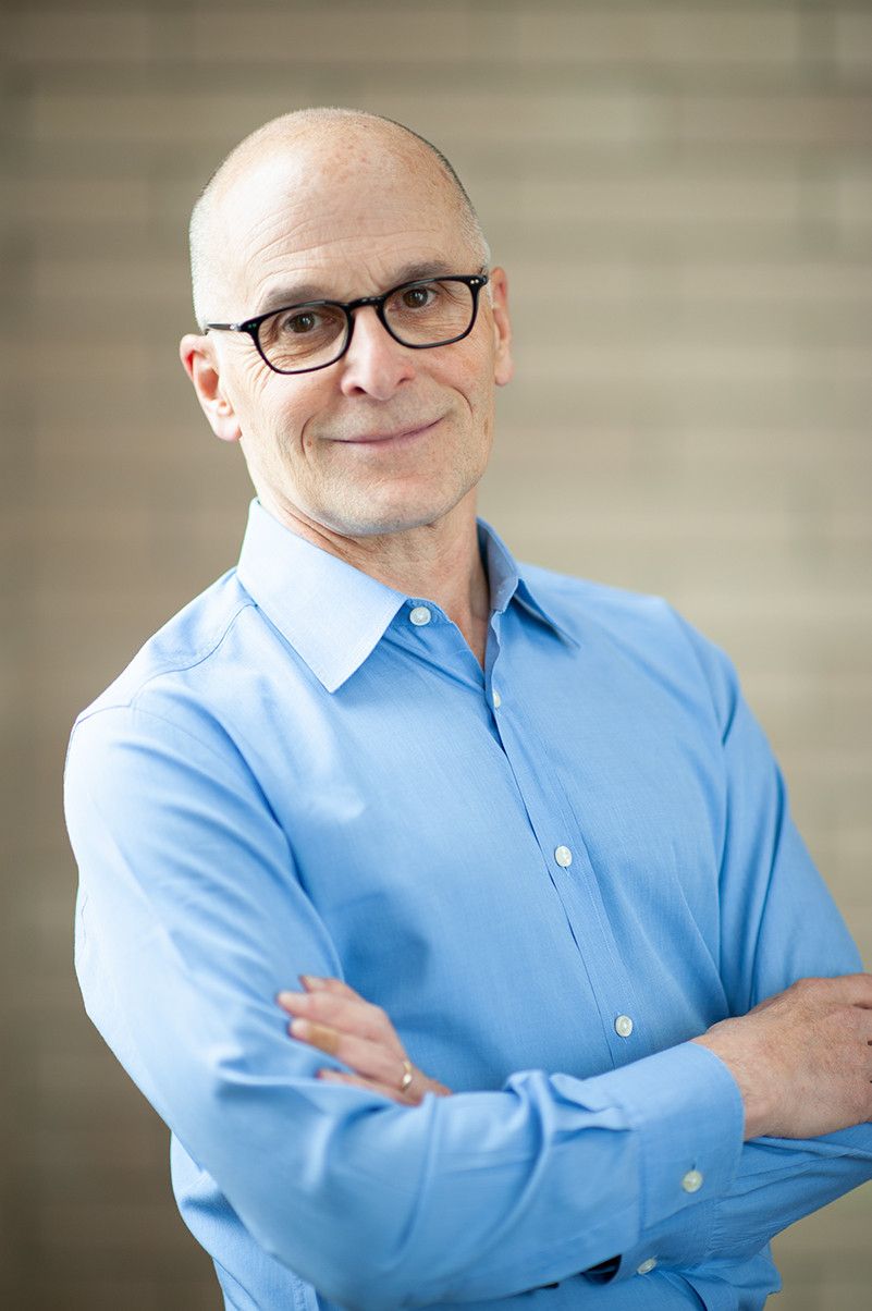 George DeMartino professional headshot, smiling with arms crossed in blue shirt