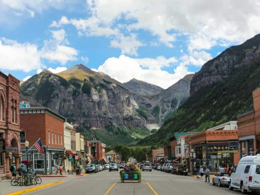 Main street of small mountain town with cars and shops, dramatic rocky peaks background
