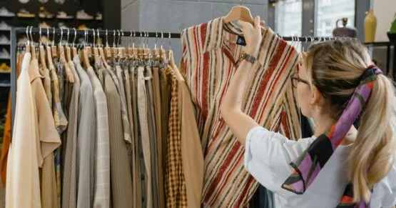 Woman browsing clothing rack in boutique store, selecting striped top {{brizy_dc_image_alt imageSrc=