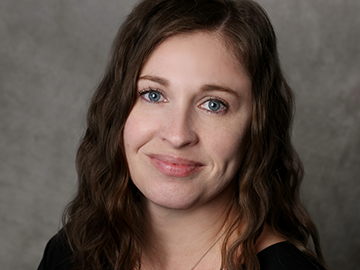 Fawn Romero professional headshot, smiling woman with wavy hair on gray backdrop