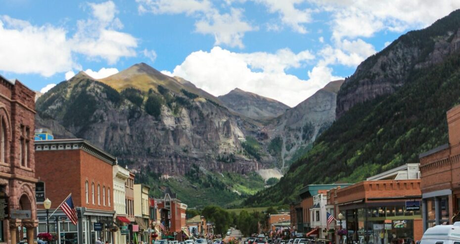 Main street of small mountain town with cars and shops, dramatic rocky peaks background