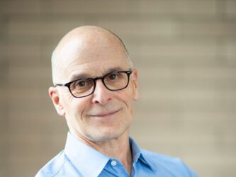 George DeMartino professional headshot, smiling with arms crossed in blue shirt