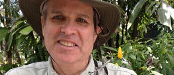 Roy Morrison smiling in safari hat and khaki shirt, lush garden background