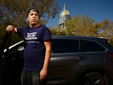 Male driver wearing Drivers Coop Colorado shirt standing by car in front of Colorado Capitol