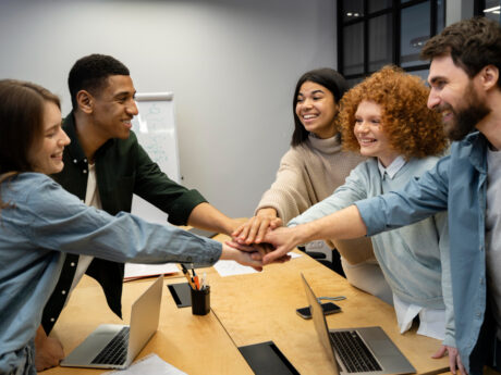 Diverse coworkers stacking hands over conference table to celebrate teamwork
