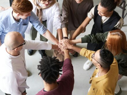 how-do-coops-work Overhead view of diverse coworkers stacking hands in unity around office table