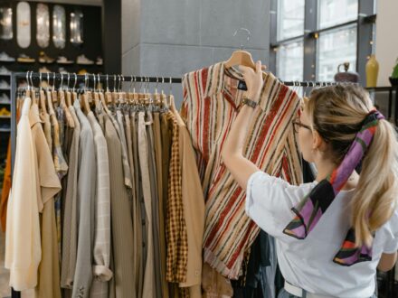 how-to-sell-your-business Woman browsing clothing rack in boutique store, selecting striped top