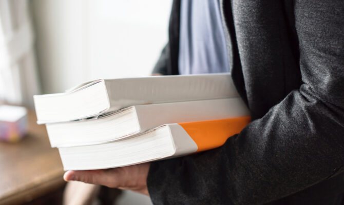 Close-up of person in blazer carrying stack of textbooks and binders