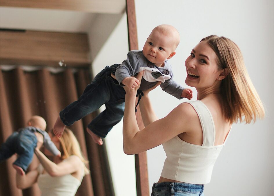 Mother lifting smiling baby in front of mirror at home