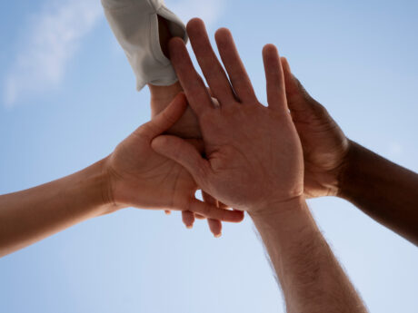 Three hands high-fiving against clear blue sky, symbolizing teamwork